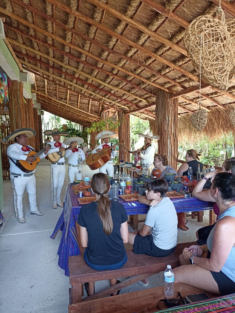 Mariachis playing for a long table of families under the palapa